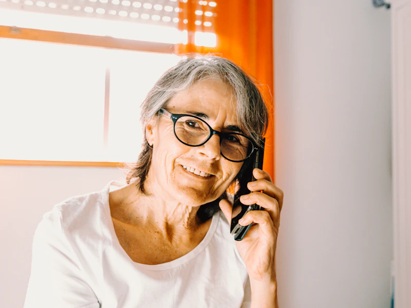 Une femme âgée souriante parle au téléphone depuis chez elle.